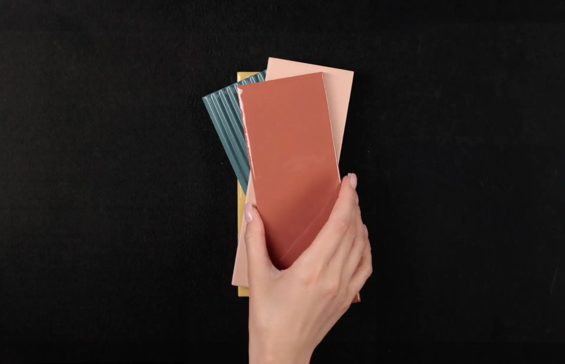 Una mano tiene pezzi rettangolari di ceramica Emilgroup di vari colori