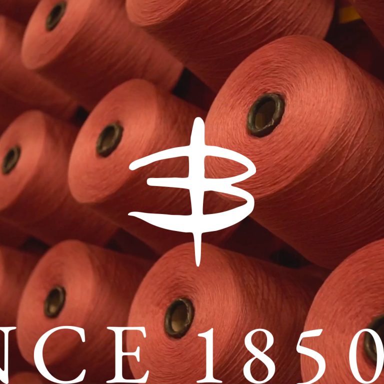 Una serie di rocchetti con filo rosso. In primo piano il logo del brand Zegna Baruffa