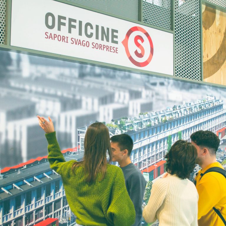 Quattro persone davanti ad una riproduzione fotografica dello stabilimento delle officine di Savigliano