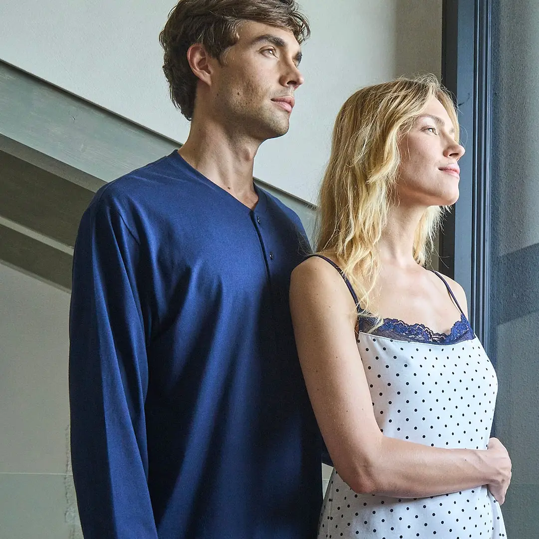 Una coppia posa con stile indossando delle camicie chic vicino a una finestra.
