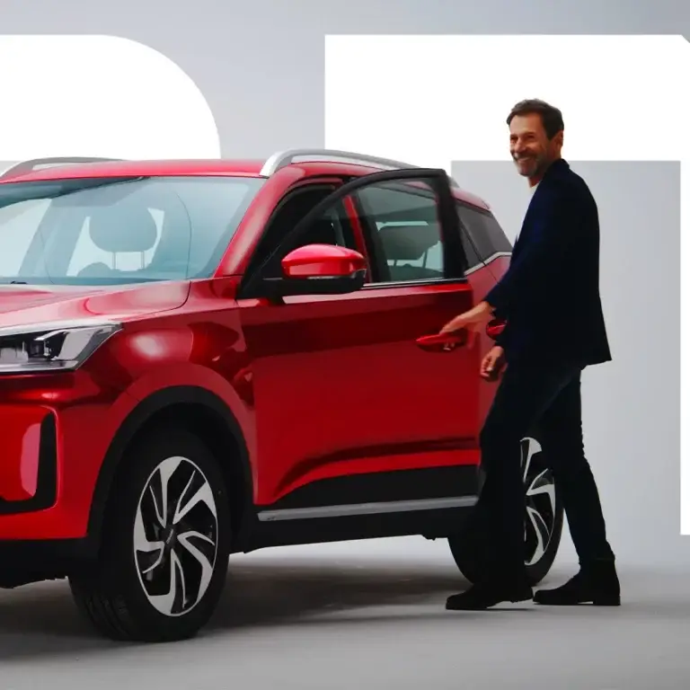 Una persona vestita di scuro sorride accanto alla portiera aperta di un SUV rosso.