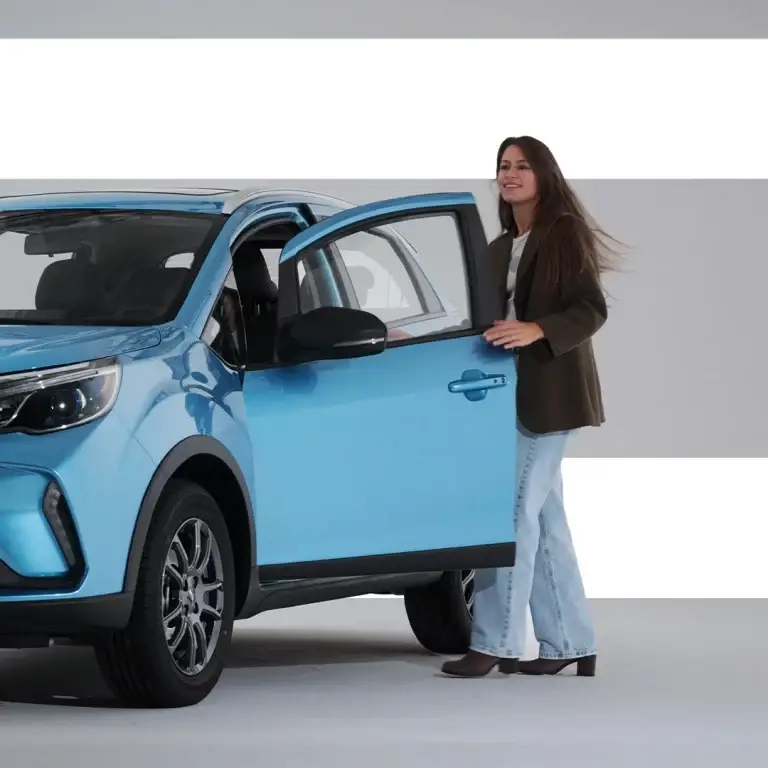 Donna in blazer e jeans accanto alla portiera aperta di un SUV azzurro.