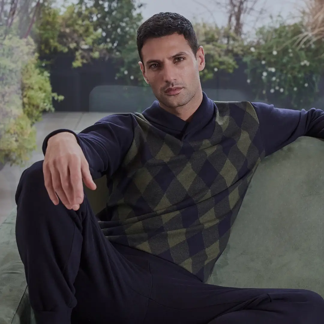 Un uomo in maglione si rilassa sul divano, confondendosi con le piante.