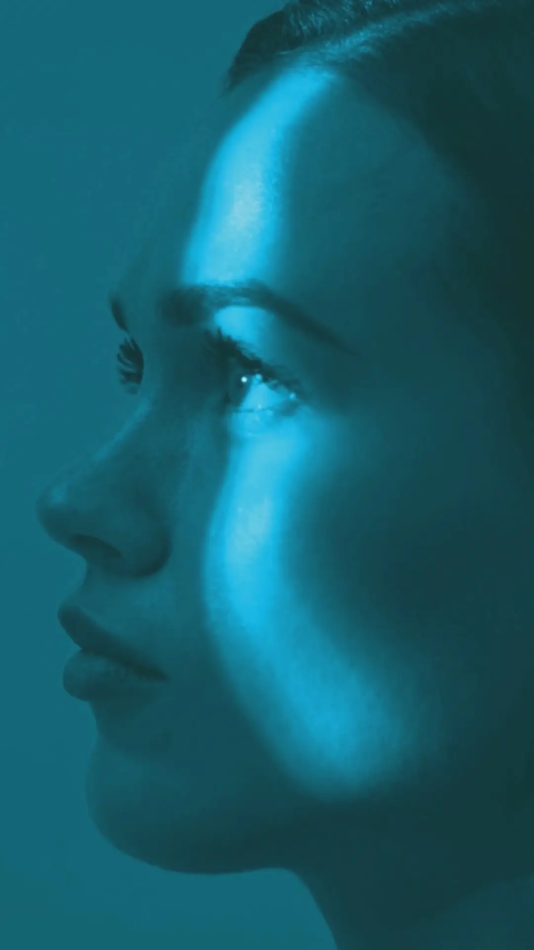Woman’s profile in blue light with bright stripe on her face.