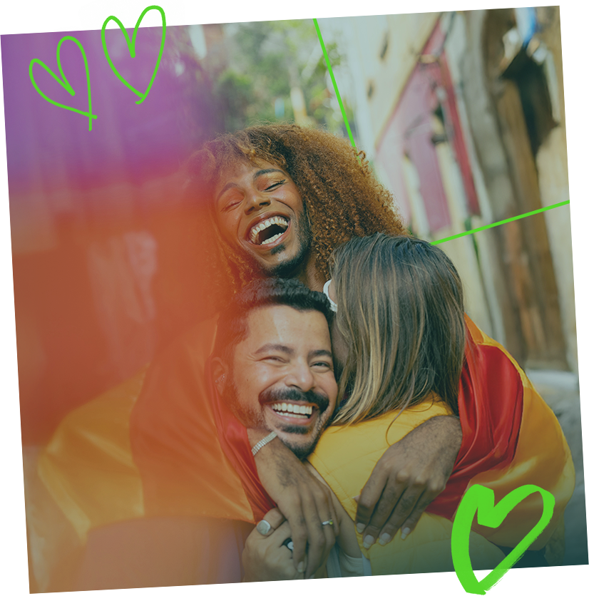 Tre persone si abbracciano in una bandiera arcobaleno, sorridendo con cuori verdi.