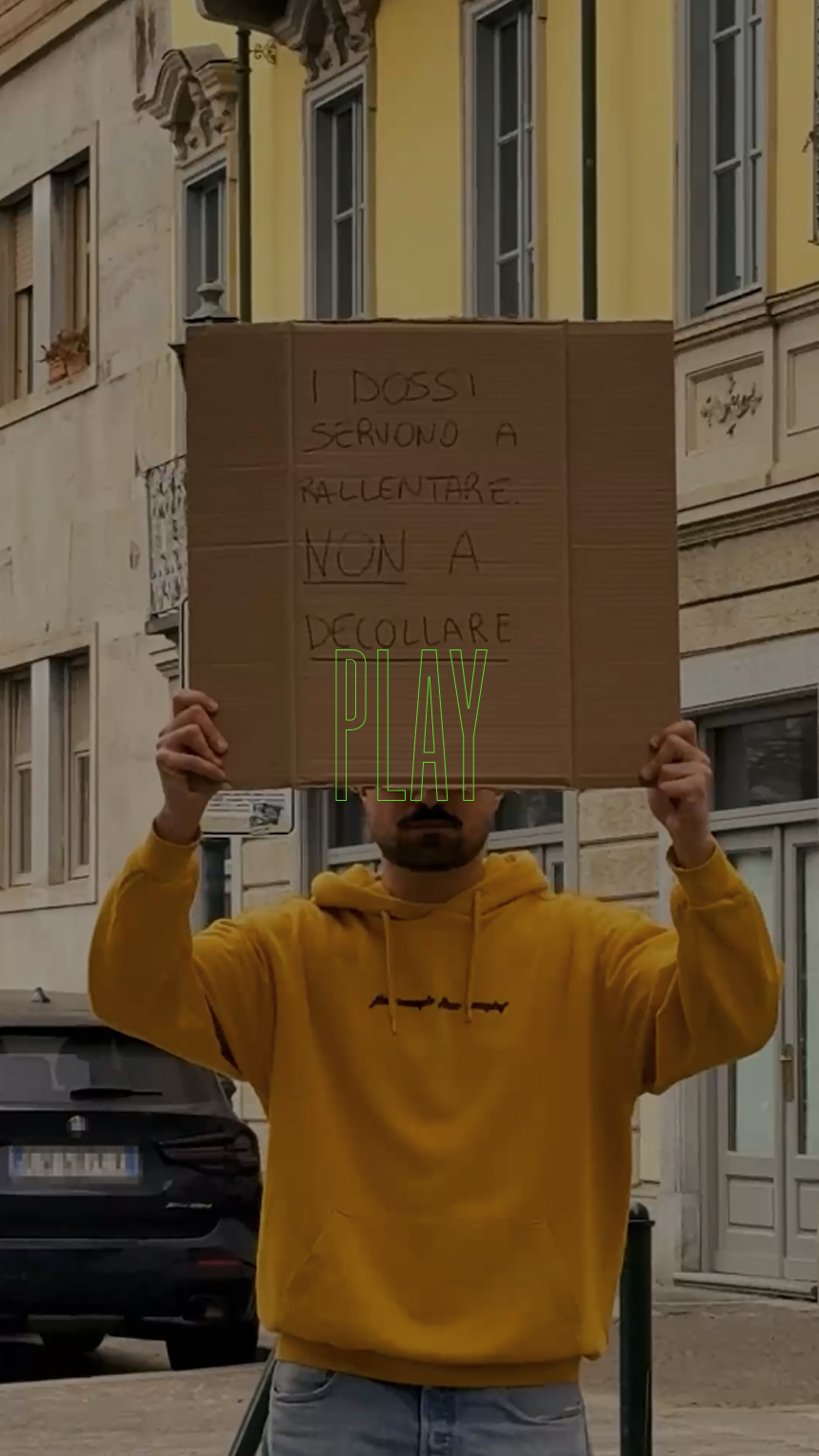Una persona in felpa gialla tiene un cartello italiano in una strada della città.
