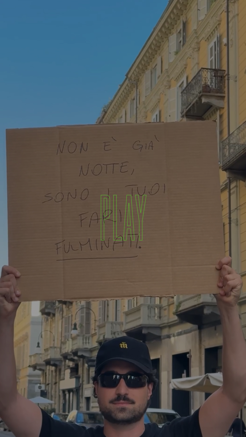 Una persona con occhiali da sole e berretto tiene un cartello di avvertimento italiano sulla strada.