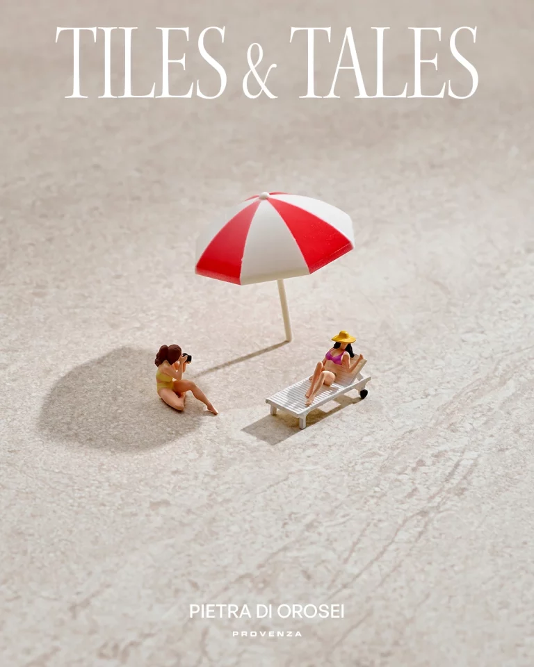 Due piccole donne si rilassano sotto un ombrello bianco-rosso su piastrella; testo: Tiles & Tales, Pietra di Orosei.