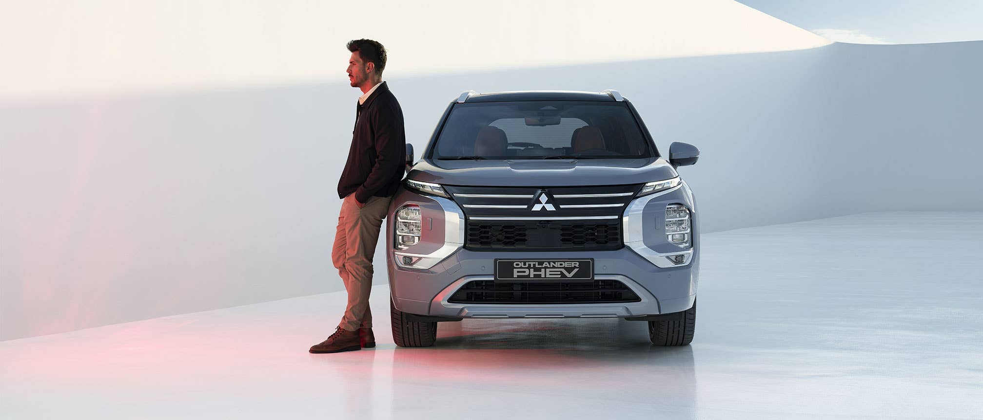 Un uomo si appoggia a una Mitsubishi Outlander PHEV argentata in uno spazio luminoso.