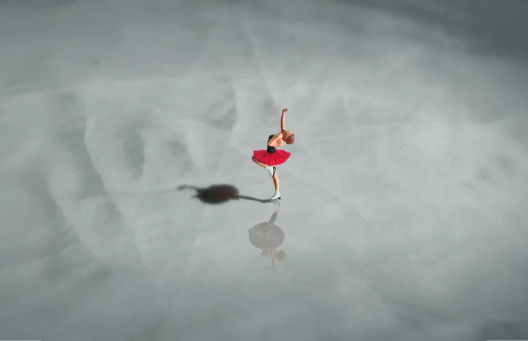 Figure skater in red spins on ice, shadow and reflection visible.