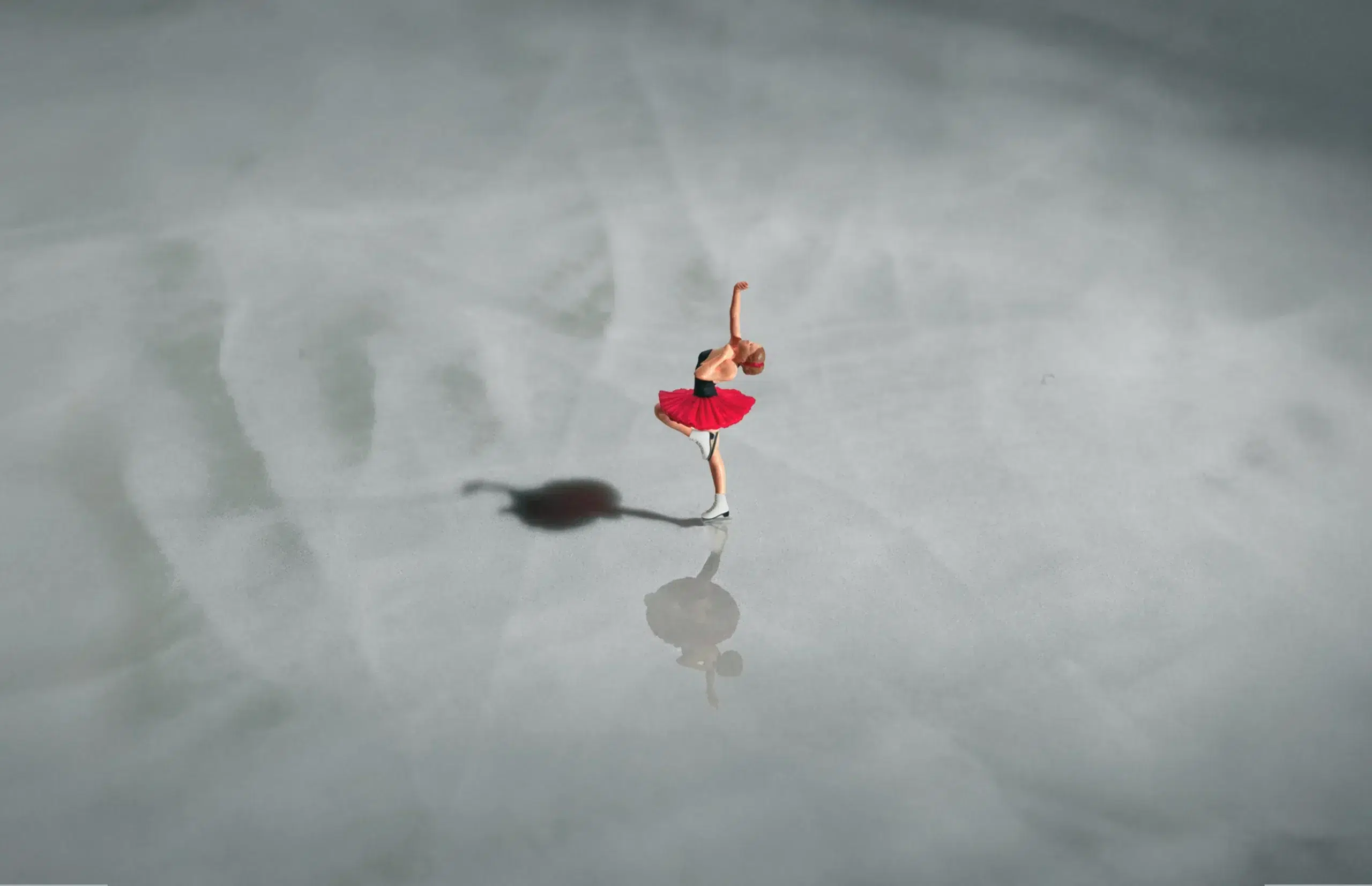 Figure skater in red spins on ice, shadow and reflection visible.